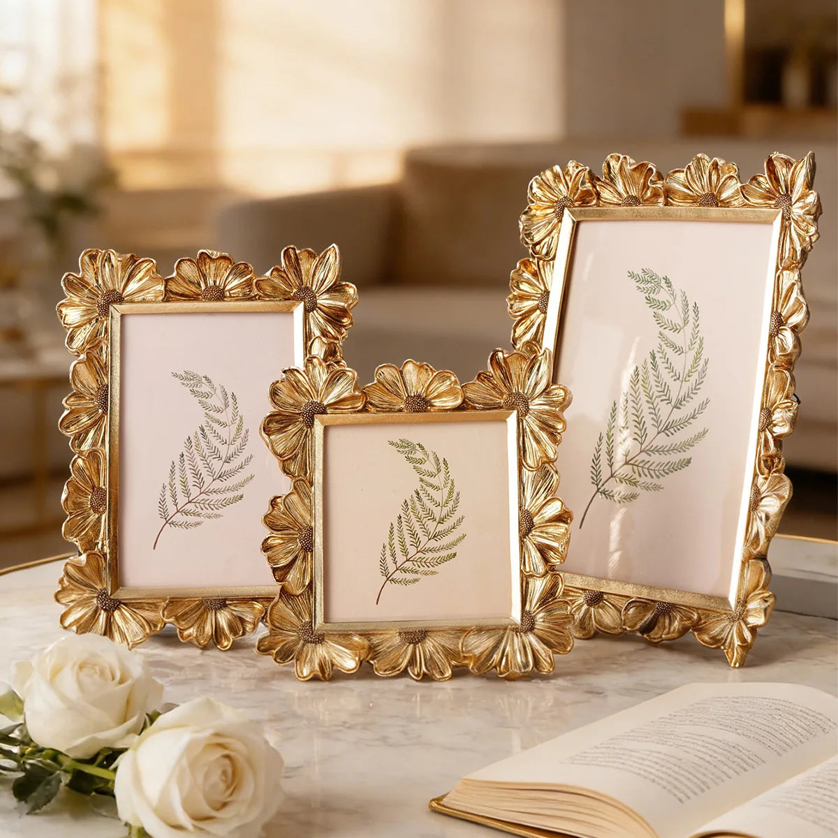 A set of three golden resin photo frames featuring elegant floral designs and greenery on a marble surface.
