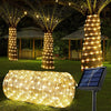 A long, cylindrical solar-powered LED rope light illuminates a grassy outdoor area with warm yellow lights.