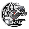A black wall clock with a design featuring text like Kitchen is the Heart of the Home and a clock face.
