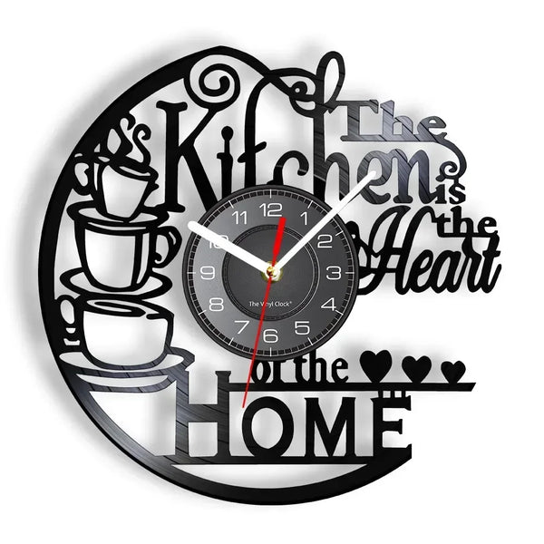 A black wall clock with a design featuring text like Kitchen is the Heart of the Home and a clock face.