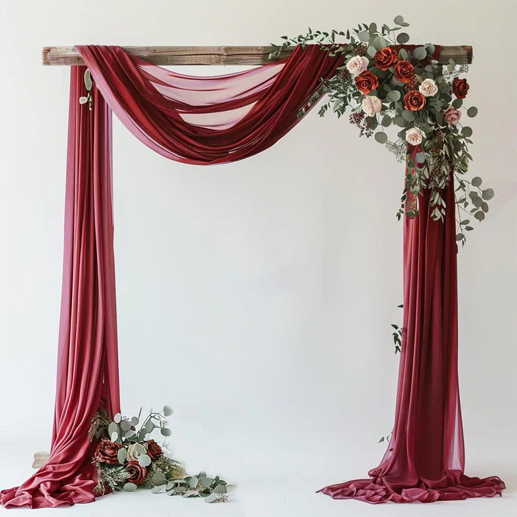 A draped archway setup featuring rich burgundy chiffon fabric and floral greenery for a wedding or event backdrop.
