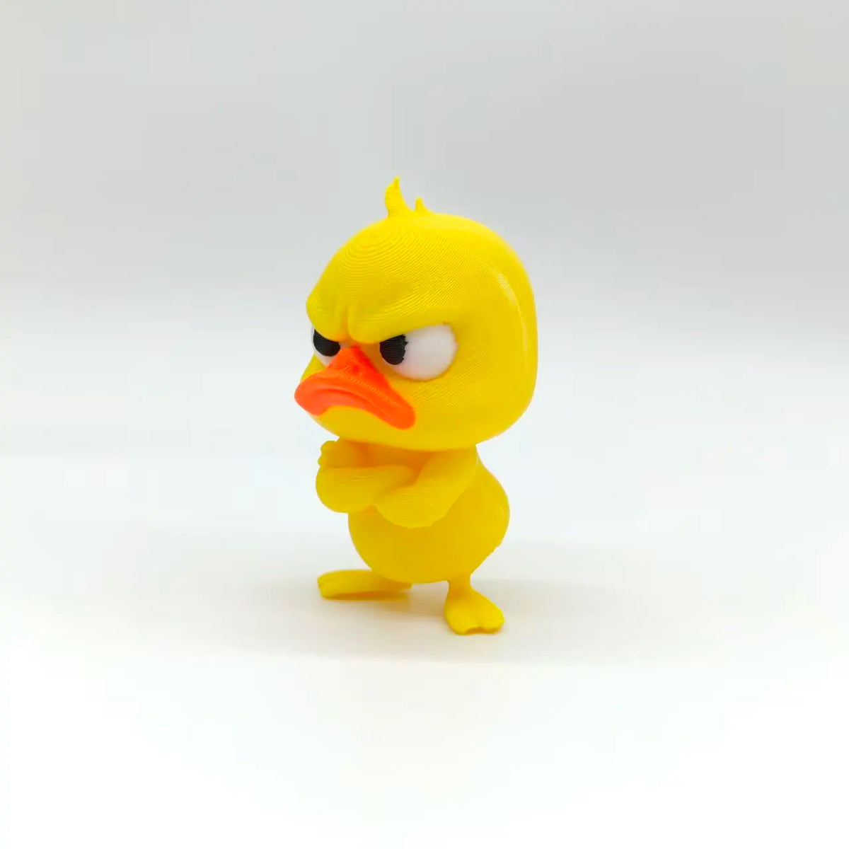 A yellow 3D printed statue of an angry duck with glaring eyes and an orange beak.