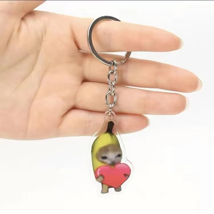 A silver acrylic keychain featuring a cute yellow banana cat with a red heart.
