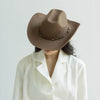 A woman wearing a brown wool cowboy hat with a studded leather band and a white collared shirt.