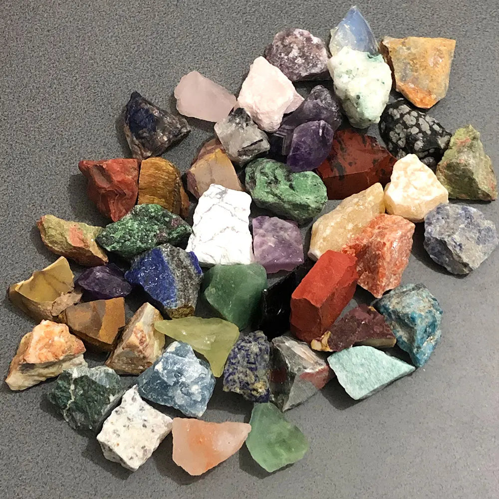 A collection of assorted natural raw crystal stones in various colors including pink, purple, green, and orange.