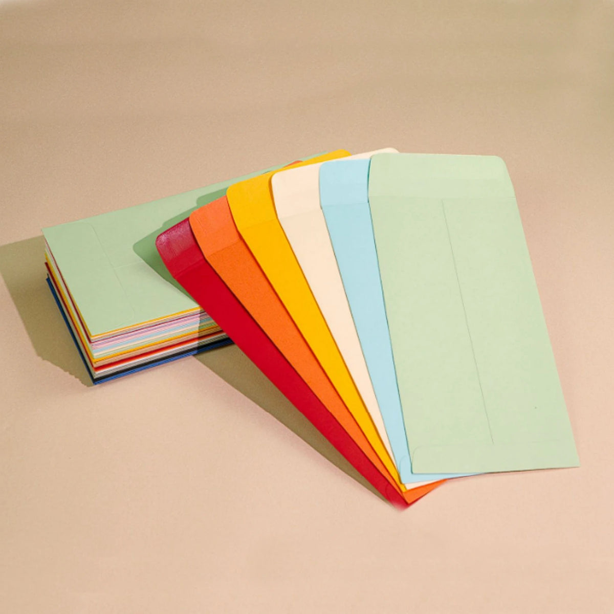 A stack of colorful side-loading cash envelopes in shades of green, orange, and blue lying on a beige surface.