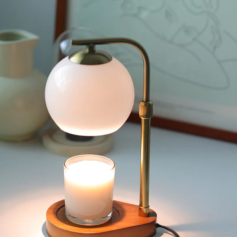 A brass aromatherapy wax melting lamp with a white spherical light illuminates a candle on a wooden base.