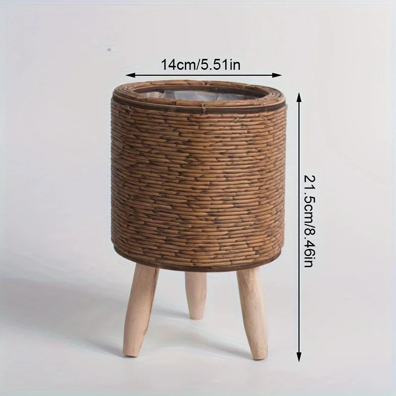 A rustic rattan planter with a round woven top and wooden legs, measuring 14cm in diameter.