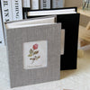 A gray linen cover photo album with a floral design, shown open next to a black folder.