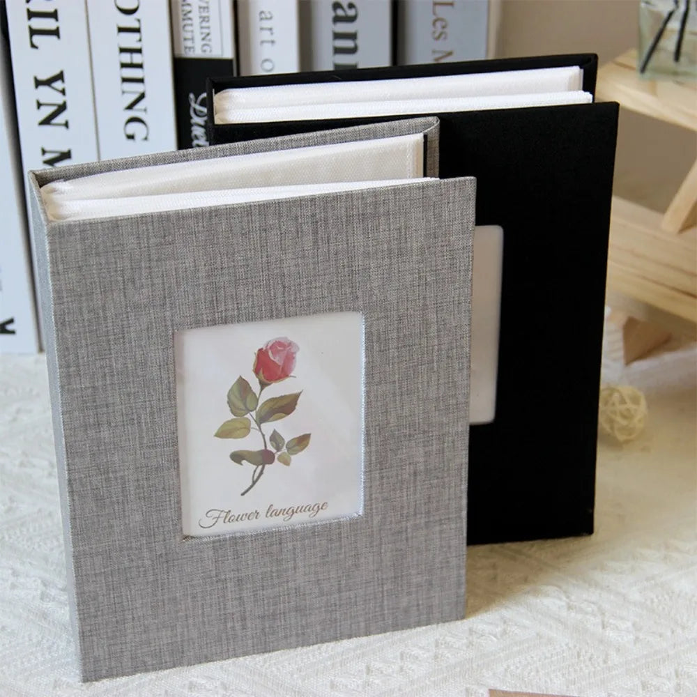 A gray linen cover photo album with a floral design, shown open next to a black folder.