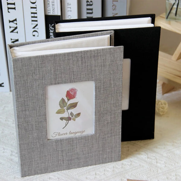 A gray linen cover photo album with a floral design, shown open next to a black folder.