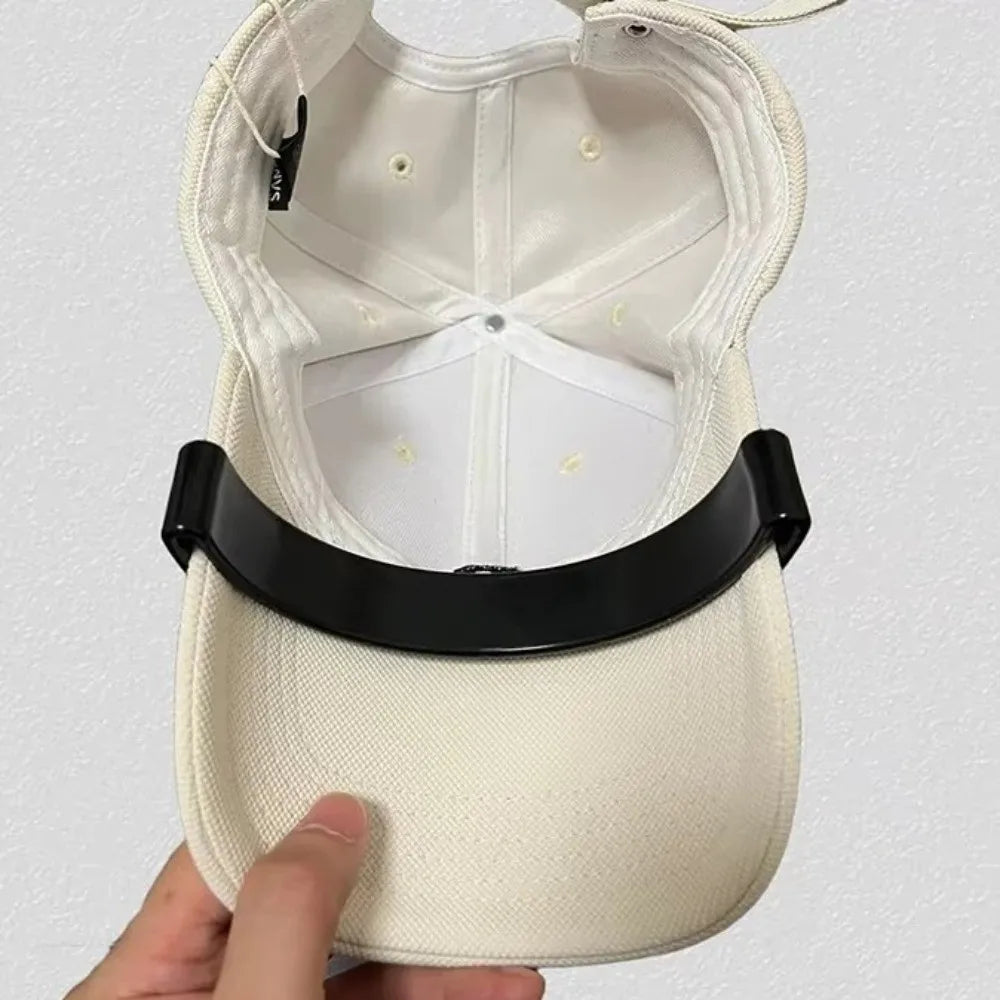 A close-up of a white adjustable hat brim shaper tool being held by a hand.