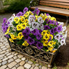 A vibrant bouquet of artificial pansy and daisy flowers in purple, yellow, and white displayed in a metal planter.