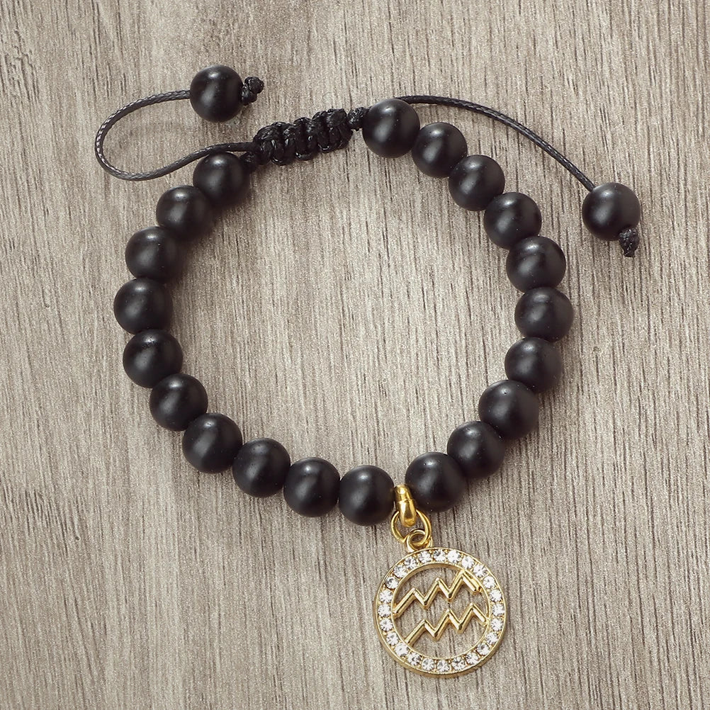 A black beaded bracelet with a gold charm featuring a line art mountain design.