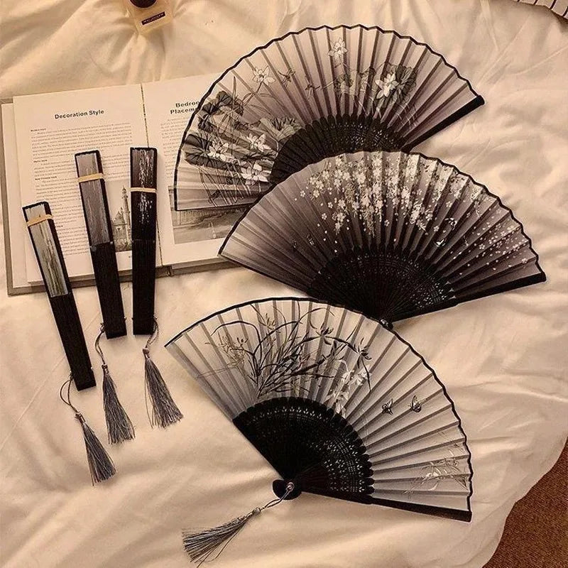 A black bamboo folding hand fan displayed on a white cloth next to informational text.