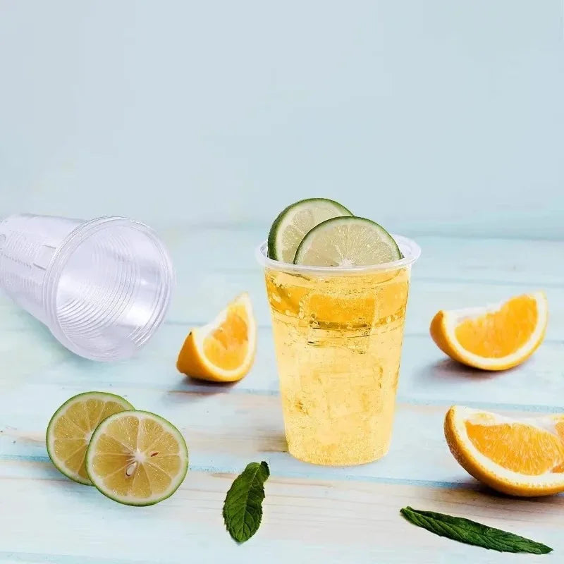 A glass of yellow citrus drink with lime slices and orange slices on a light wooden surface.