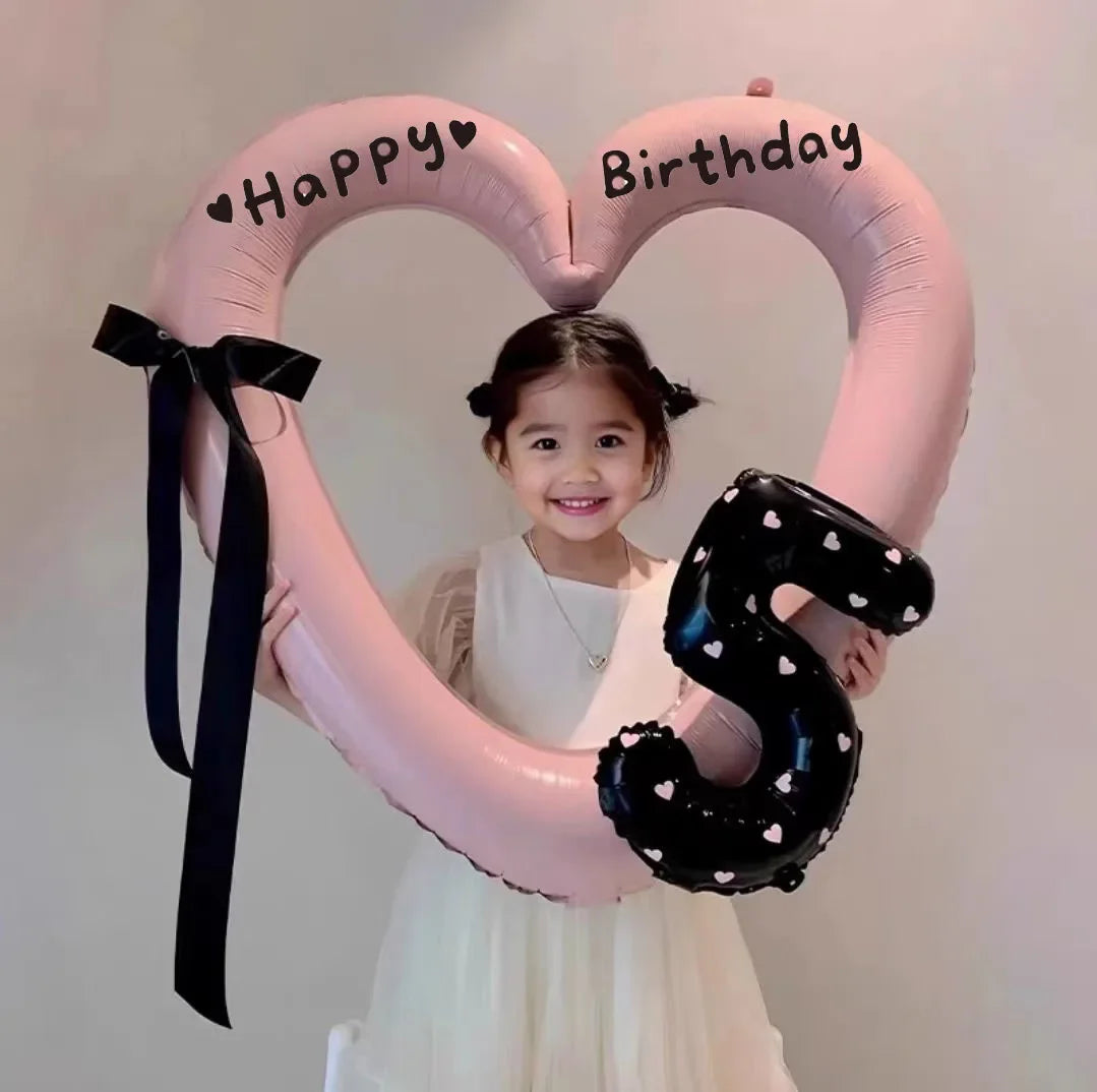 A young girl is holding a large pink heart balloon decoration with Happy Birthday written on it.