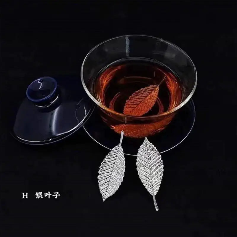 Sterling silver tea brewing leaves resting on a glass of amber liquid.