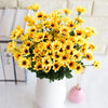 A bouquet of bright yellow artificial sunflowers in a white vase with pink ribbon