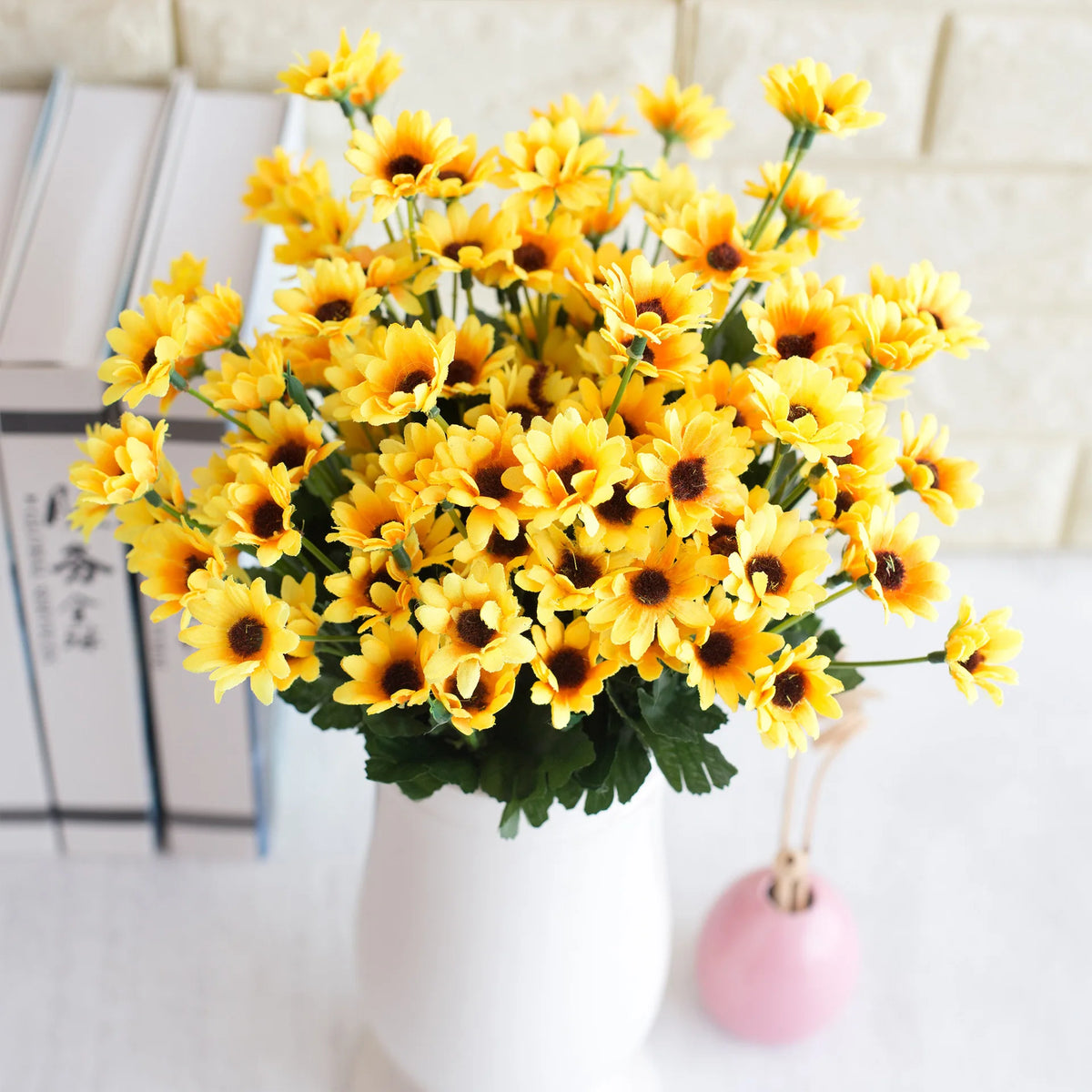 A bouquet of bright yellow artificial sunflowers in a white vase with pink ribbon
