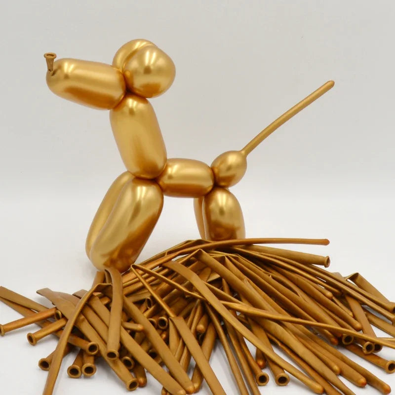A golden latex modeling balloon shaped like a stylized animal standing on a pile of thin, gold-colored straws.