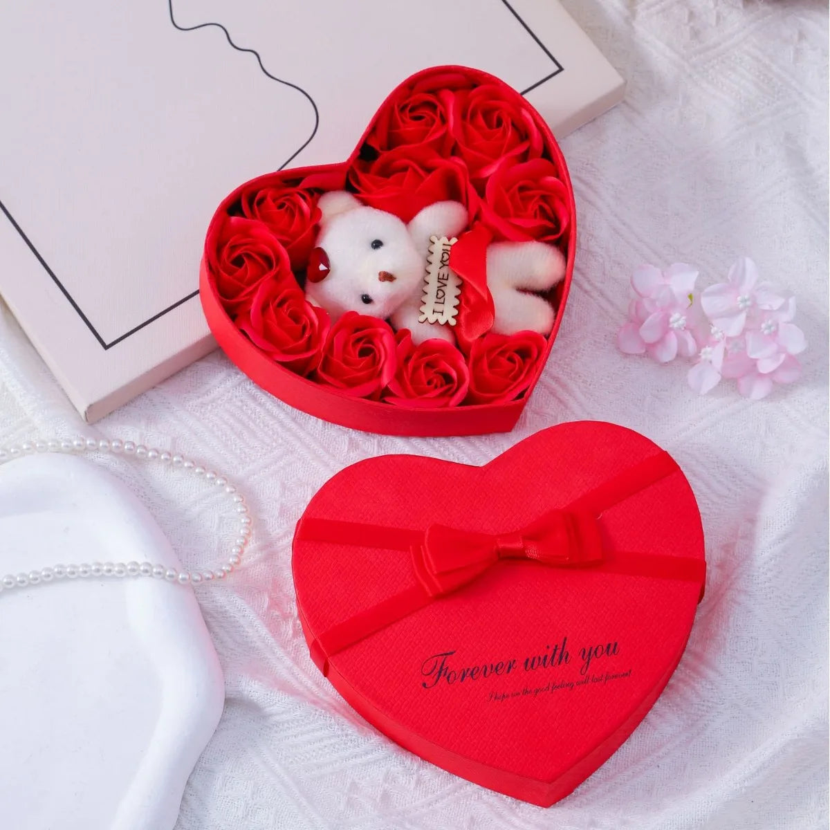 A red heart-shaped gift box filled with artificial roses and a white plush bear