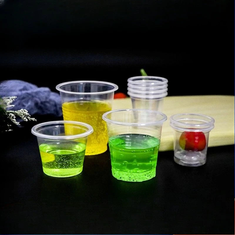 A collection of disposable mini tasting cups filled with various colored liquids, including yellow, green, and clear, set aga