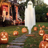 A white ghost decoration hangs in the air in a garden setting surrounded by carved pumpkin decorations.