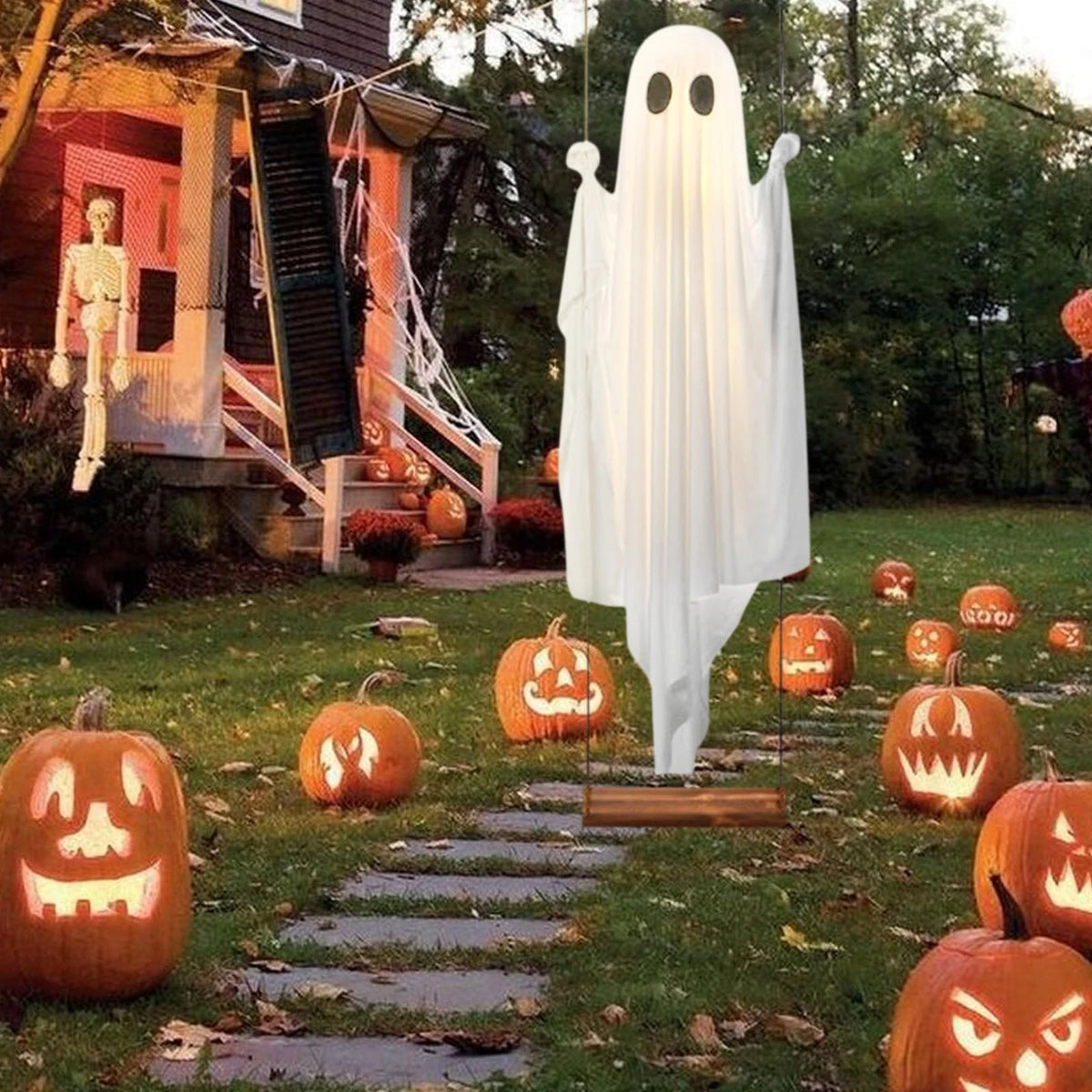 A white ghost decoration hangs in the air in a garden setting surrounded by carved pumpkin decorations.