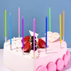 A pink birthday cake decorated with colorful thin candles and fresh strawberries.
