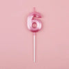 A pink number six candle on a stick against a light pink background.