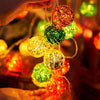 A hand is holding a string of festive LED fairy lights decorated with colorful, shimmering spherical ornaments.