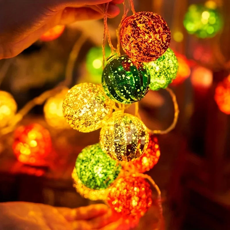 A hand is holding a string of festive LED fairy lights decorated with colorful, shimmering spherical ornaments.