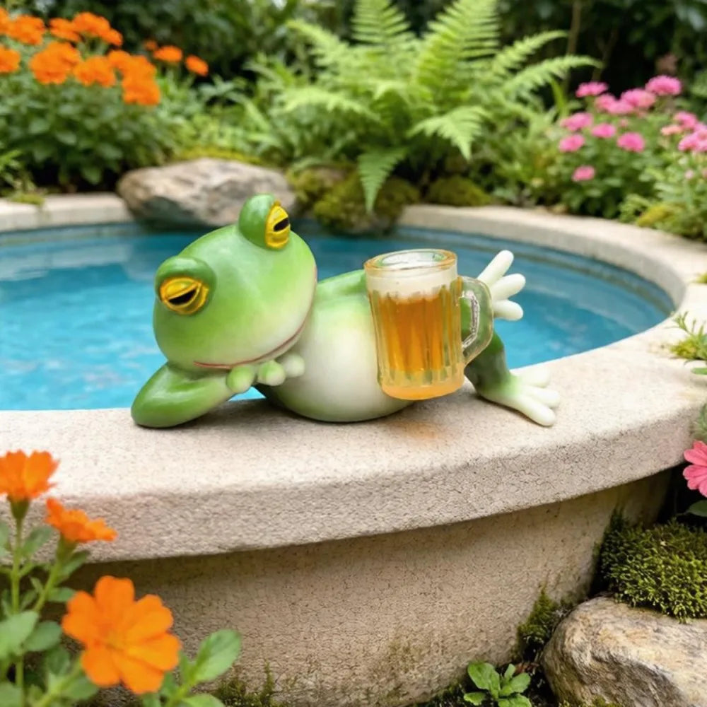 Figura de rana de resina verde sentada en un saliente de piedra junto a un vaso de líquido ámbar en un jardín.