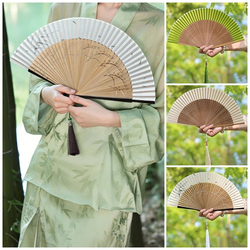 A woman holds an elegant bamboo folding fan with a tassel in various shades of green and natural wood tones.