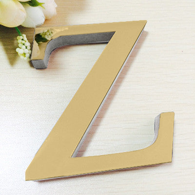 A gold letter Z cutout for a mirror wall decal set resting on a light wooden surface with white flowers.