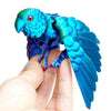 A hand holds an articulated 3D printed parrot figurine with vibrant blue wings.