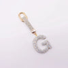 A gold-toned letter G keychain charm covered in clear crystals.