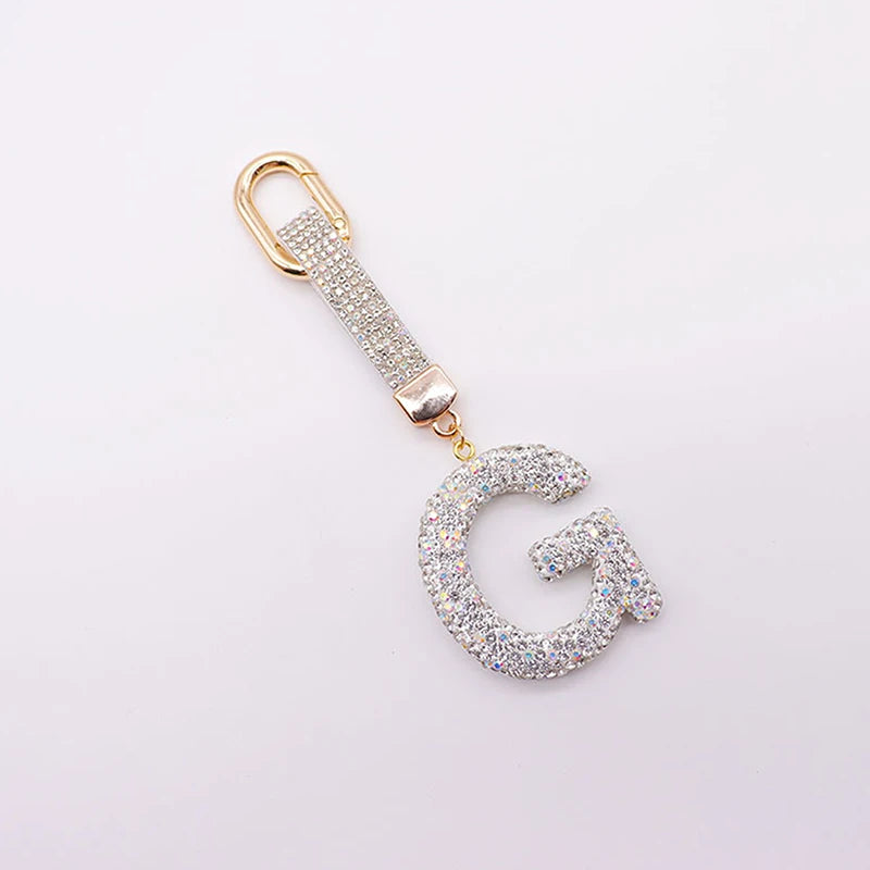 A gold-toned letter G keychain charm covered in clear crystals.