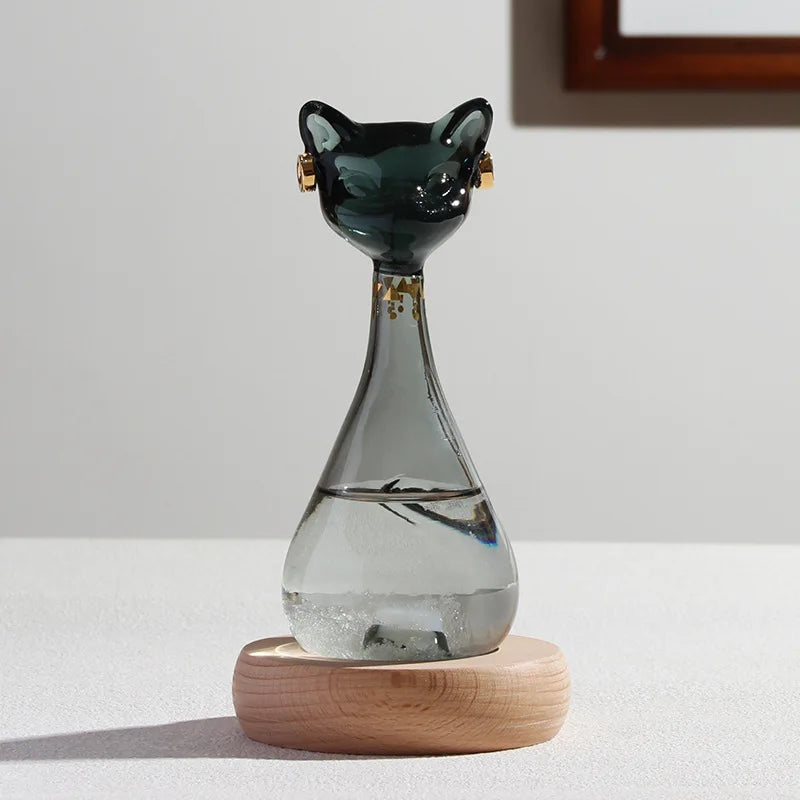 A glass bottle shaped like an Egyptian cat with gold accents, resting on a wooden base.