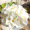 A bouquet of five white calla lily blooms with yellow centers arranged on a light surface.