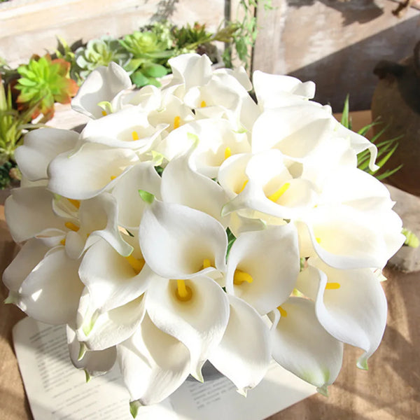 A bouquet of five white calla lily blooms with yellow centers arranged on a light surface.