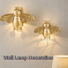 Goldene Bienenwandlampe mit geschnitzten Bienen, die Schatten auf eine weiße Wand werfen.