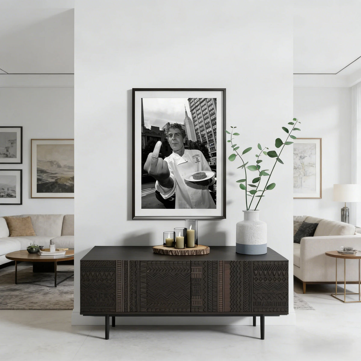 Black framed portrait of Anthony Bourdain in a white shirt displayed on a dark wood console table.