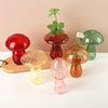 A collection of mushroom-shaped glass vases in translucent colors, including red, amber, pink, and green, displayed on a wood