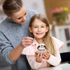 A young girl smiles while holding a handmade crochet sloth doll with a positive message card.