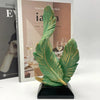 A vibrant green feather sculpture with gold accents displayed on a black base.