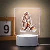 A glowing 3D LED night light depicting two hands clasped in prayer against a soft background.
