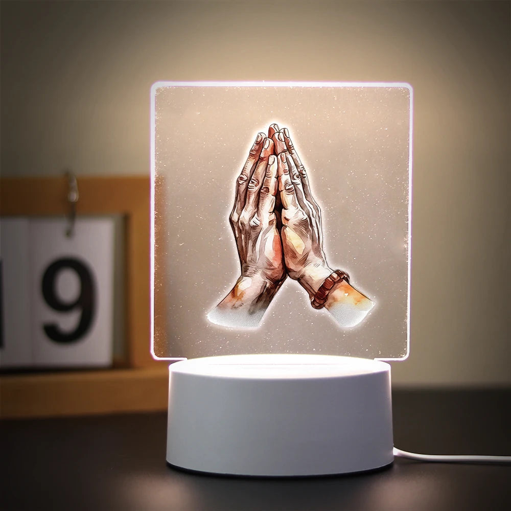 A glowing 3D LED night light depicting two hands clasped in prayer against a soft background.
