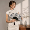 A woman holds an antique style bamboo folding hand fan in a white dress against a light background.
